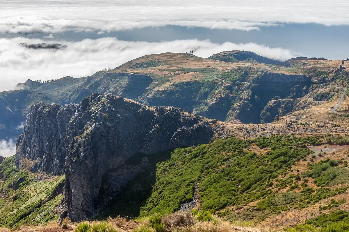 Groene bergkam van Madeira boven een wolkendek, met een smal wandelpad langs de rotswand
